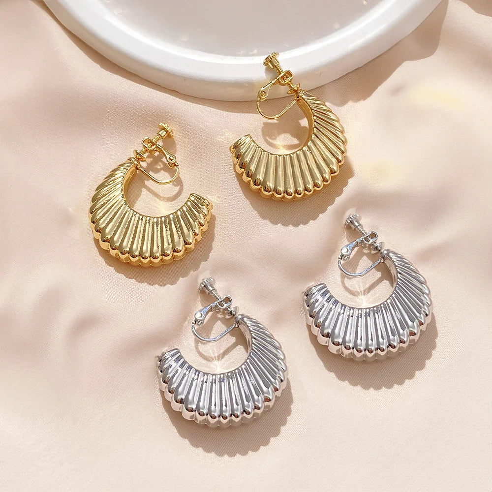 Gold and silver croissant semi hoop clip-on earrings flat lay on beige background with ceramic dish