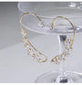 Crystal Leaf Cuff Earrings in Gold displayed on a champagne flute, showcasing the delicate cubic zirconia leaf design and curved gold wire structure from a front angle view.