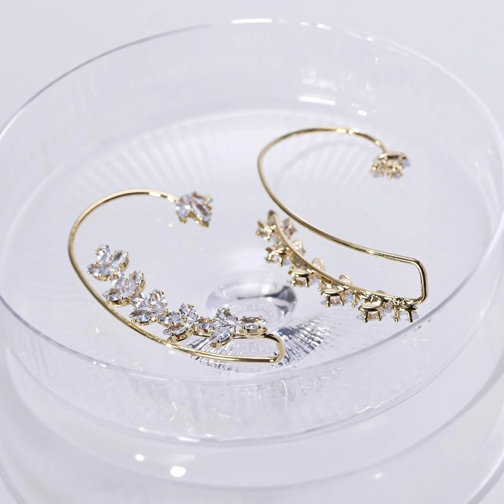 Gold Crystal Leaf Cuff Earrings displayed in clear dish, top view showing sparkly diamond-like crystals and delicate leaf design