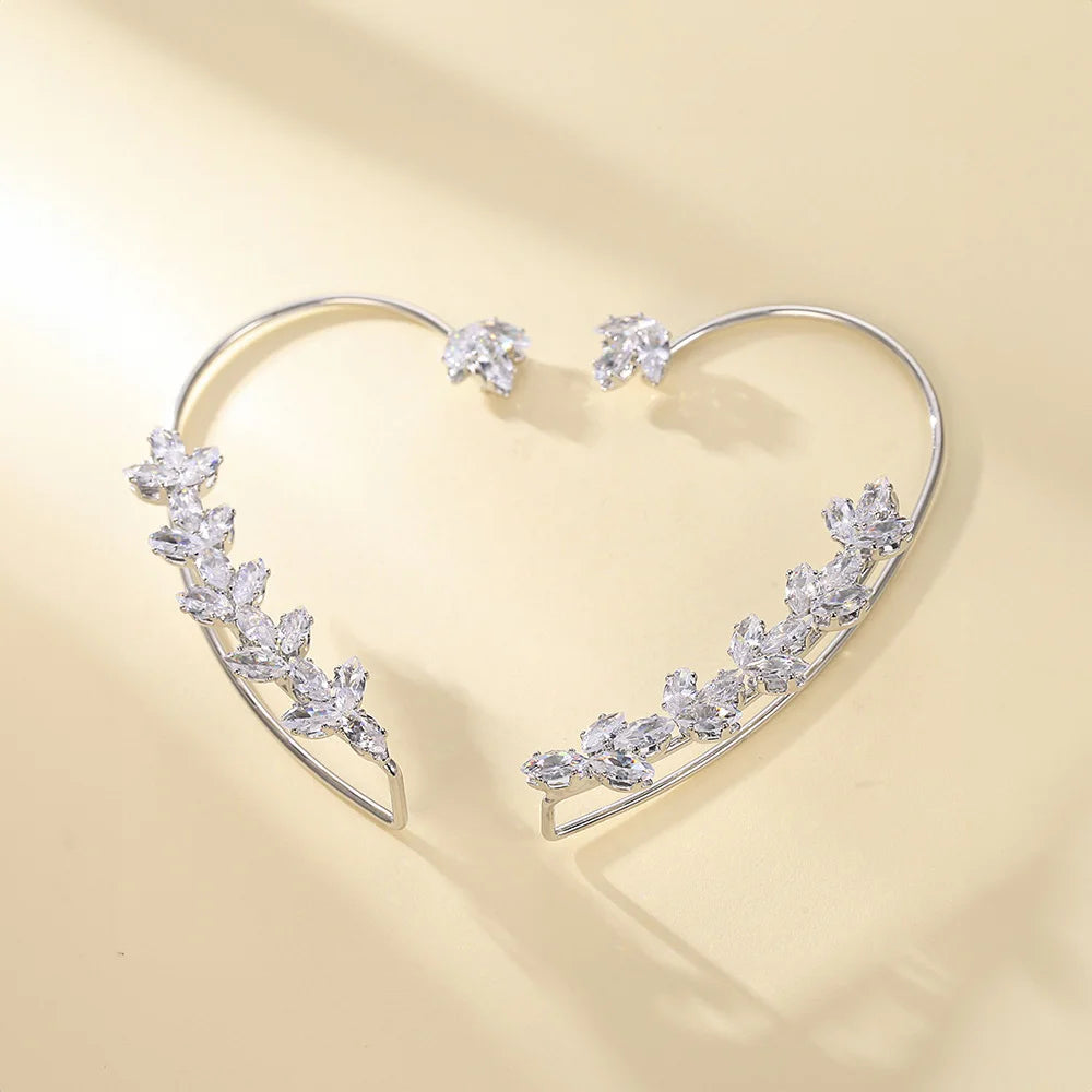 Silver crystal leaf cuff earrings displayed at an angle on a beige background, showcasing sparkling cubic zirconia details