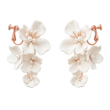 A pair of dangling floral earrings with white flower petals and small pearl-like beads, set in rose gold-tone metal, shown on a plain white background.