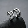 Silver double-band minimalist clip-on ear cuffs displayed on dark stone, showcasing sleek metallic design and curved structure from angled side view