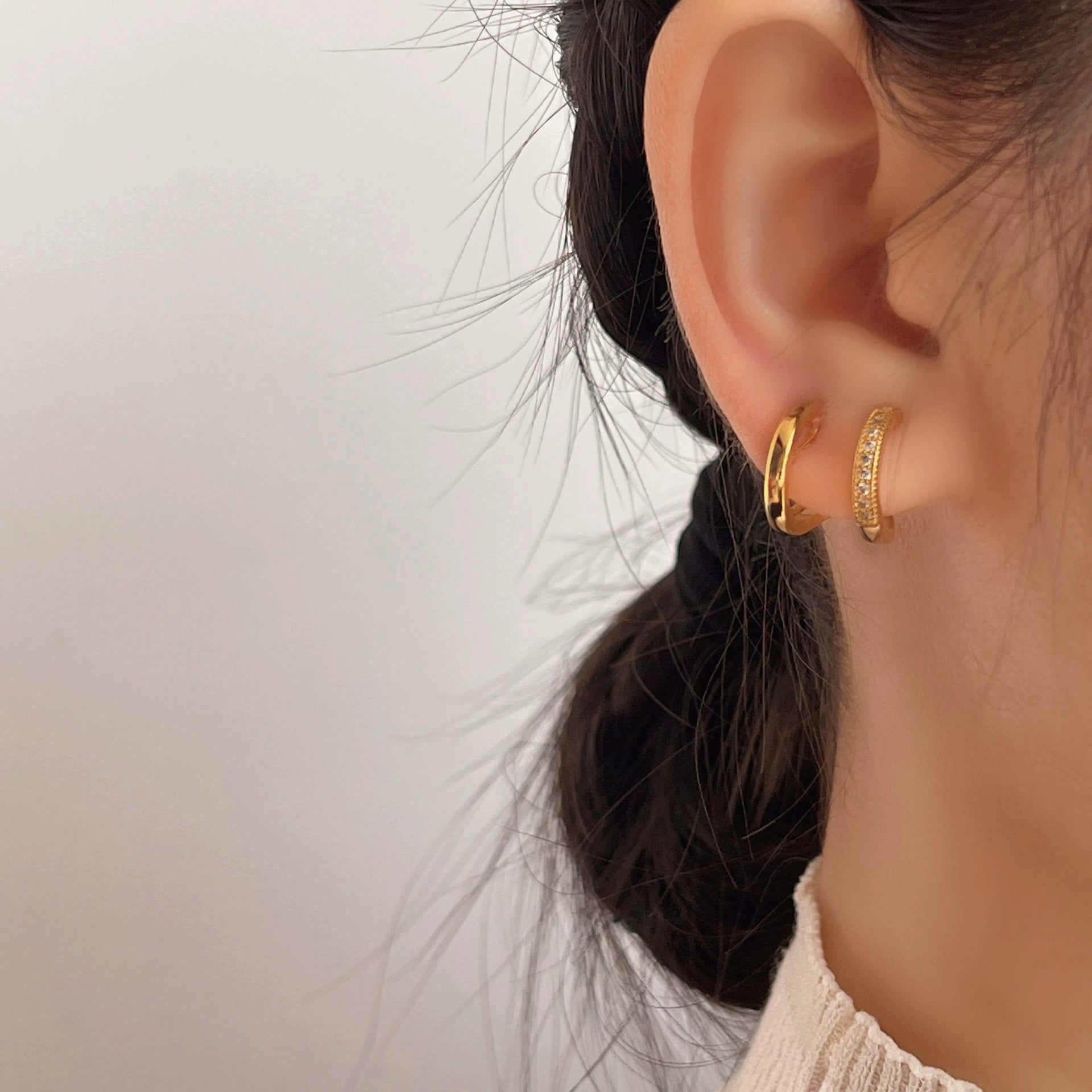 Close-up of an ear wearing gold hoop earrings with a neutral background