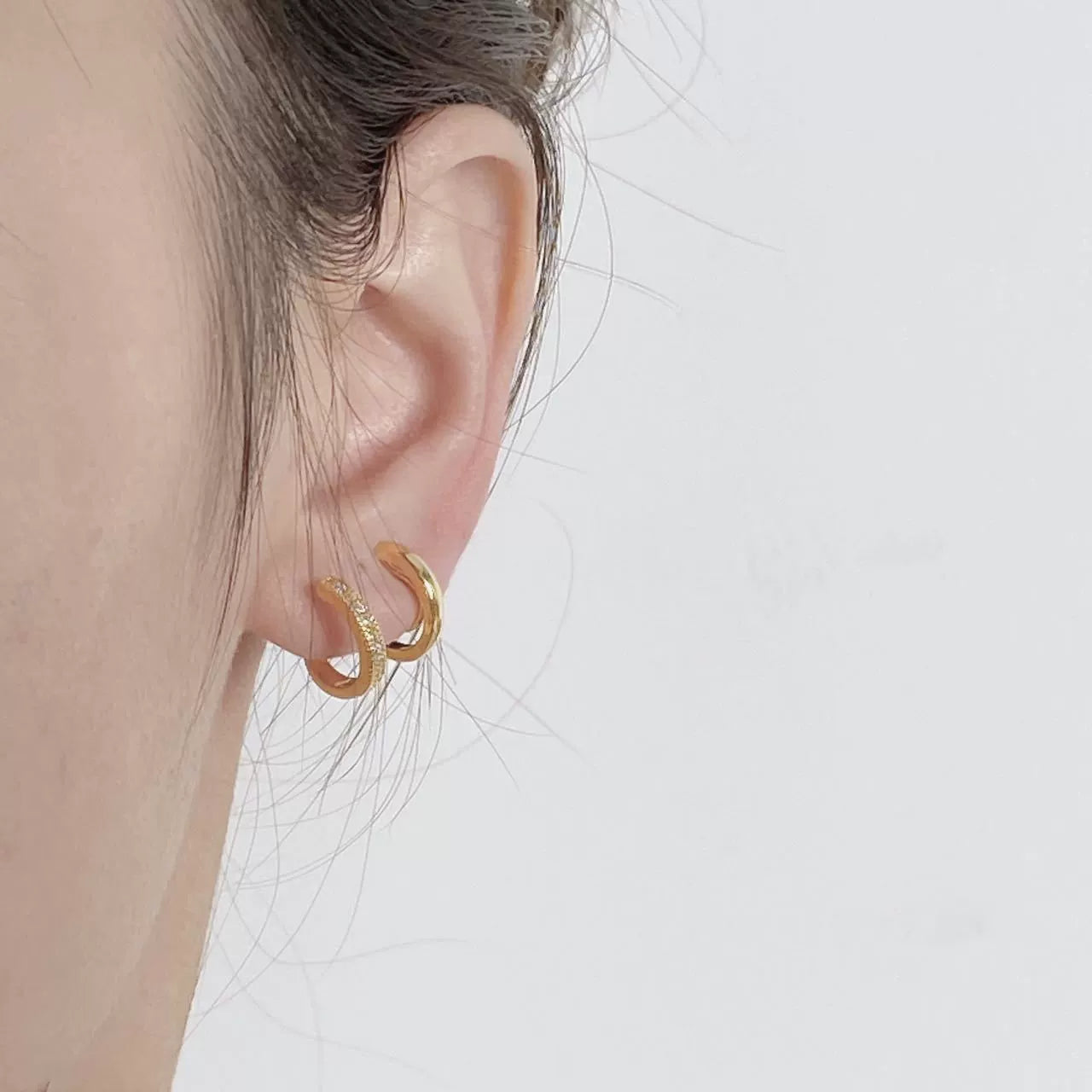 Close-up of an ear wearing gold hoop earrings on a plain background