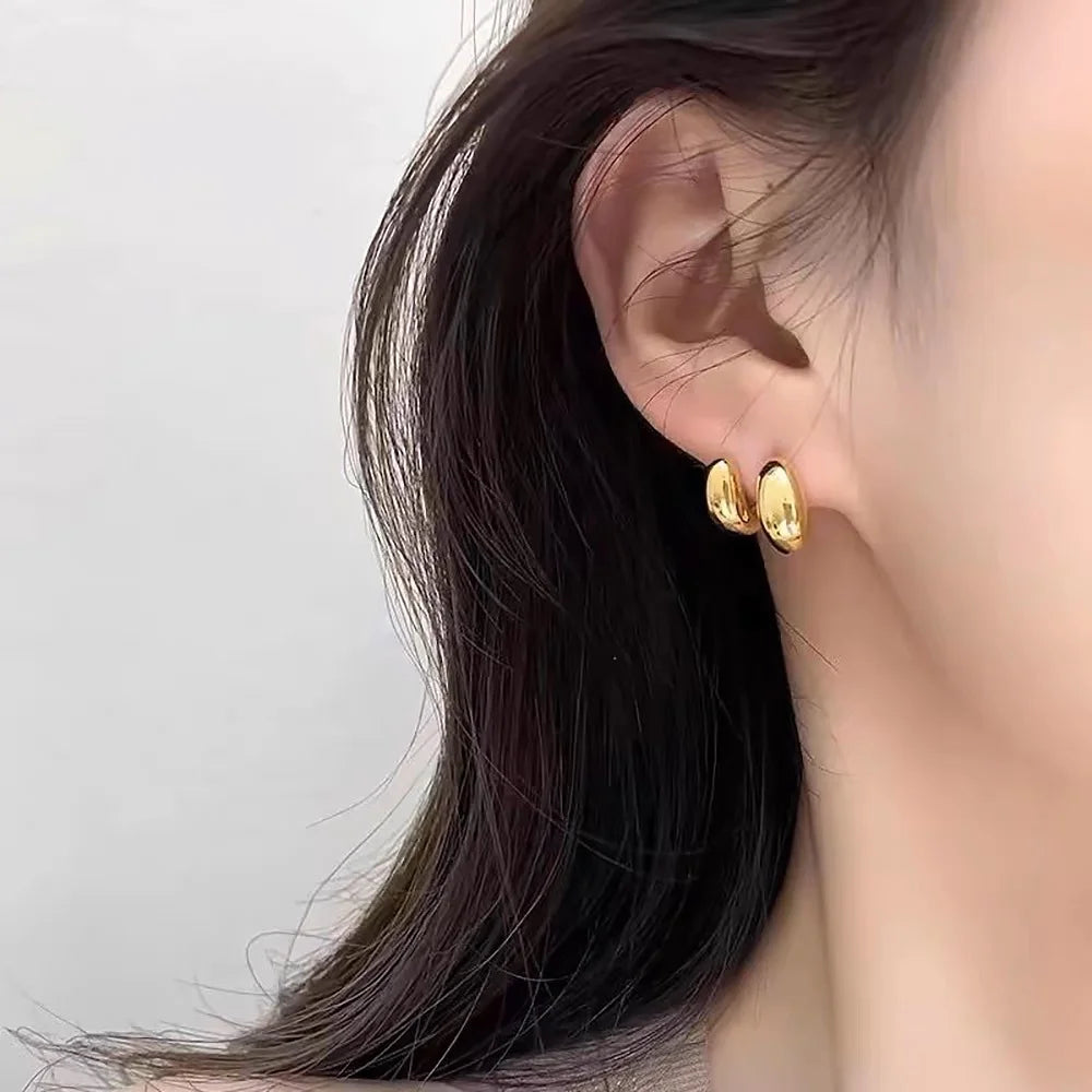 Dual bean-shaped clip-on earrings in polished gold worn on ear, side profile view