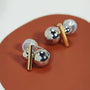 Dual-tone sphere and bar clip-on earrings displayed on terracotta surface, showcasing silver and gold metallic finish from an angled view.