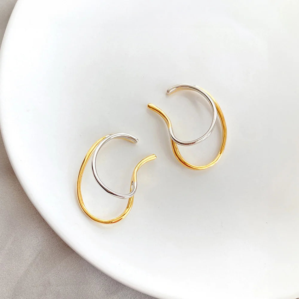 Dual-tone wave ear cuffs in gold and silver displayed on white ceramic dish, overhead view