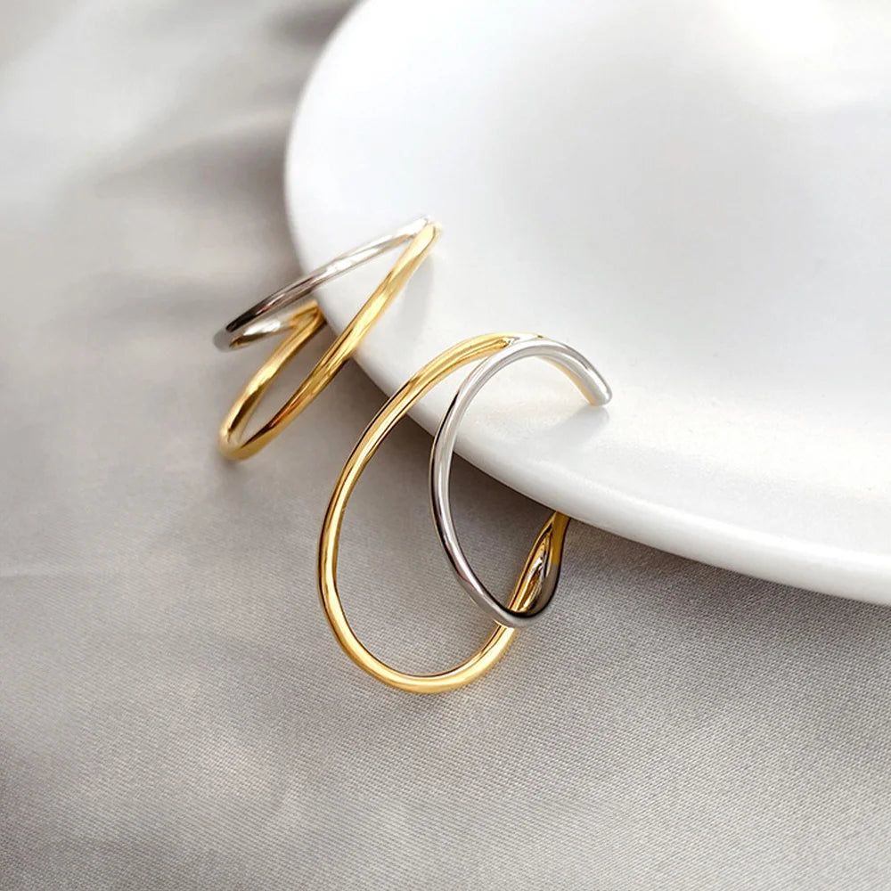 Dual-tone wave ear cuffs in gold and silver displayed on white ceramic dish, front angle view