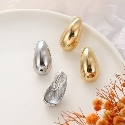 Array of minimalist chunky drop clip-on earrings in silver and gold. These bean-shaped hoops are made from a polished alloy with a hinge-back clip-on mechanism for ease of wear.