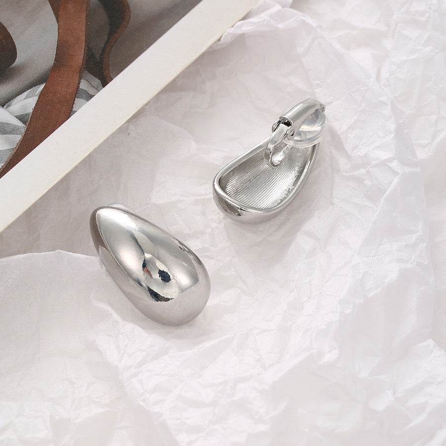 Boucles d'oreilles pendantes à clip, épaisses et de forme minimaliste en haricot, en alliage de cuivre argenté, finition polie et fermoir à charnière.
