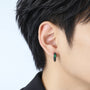 A close-up of a person's ear wearing a small black hoop earring with a green oval gemstone and textured detailing.
