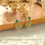 Emerald filigree dangle clip-on earrings displayed on wooden surface with dried flowers, showing gold ornate design with green stones