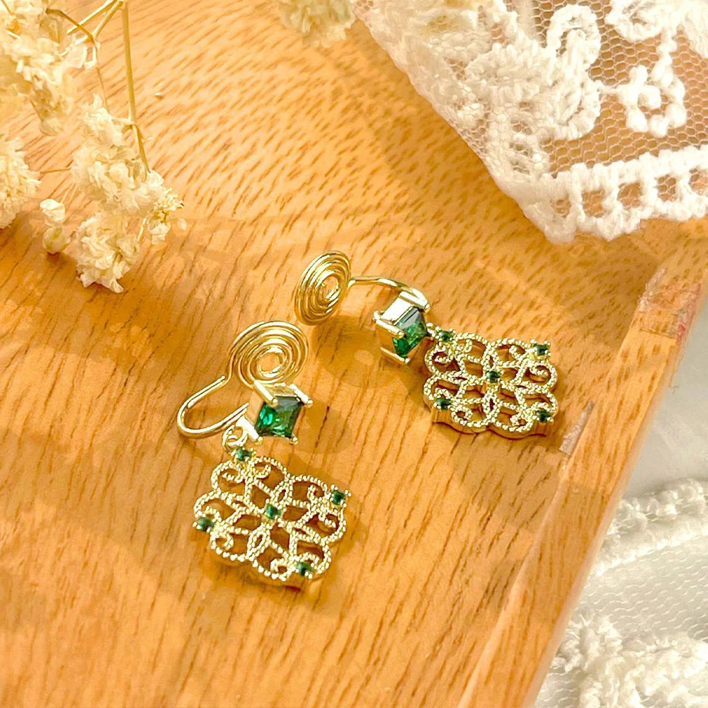 Emerald filigree dangle clip-on earrings displayed on wooden surface with lace backdrop