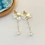 Floral pearl clip earrings with gold petals and dangling pearls on white background flat lay