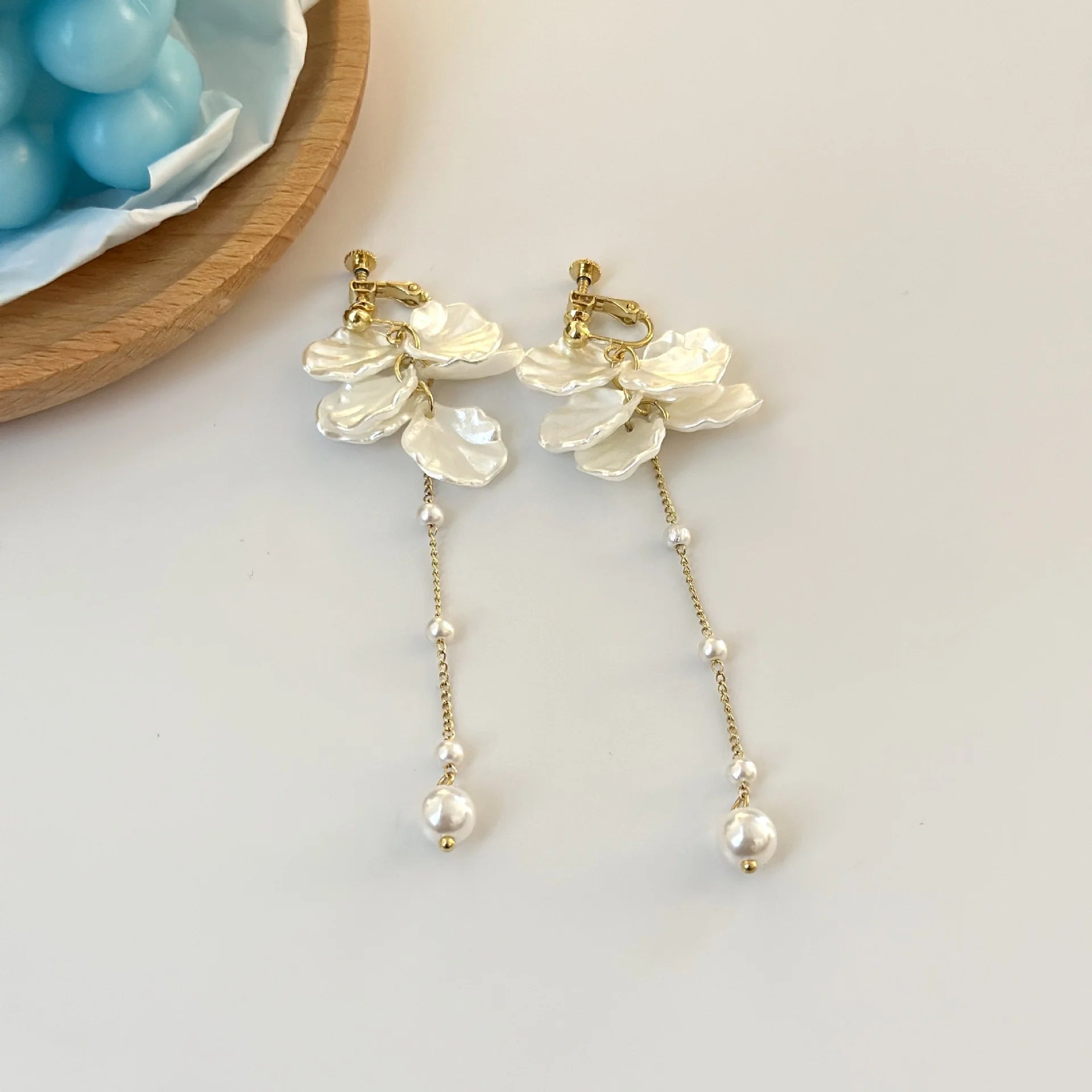 Floral pearl clip earrings with gold petals and dangling pearls on white background flat lay