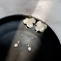 Floral pearl clip earrings with white shell flower tops and dangling pearl strands on black dish, overhead view