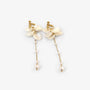 A pair of gold-toned dangle earrings featuring textured cream flower clusters, delicate chain links with small pearls, and larger dangling pearls, shown on a light gray background.