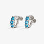 A pair of silver huggie hoop earrings featuring a vertical row of three round-cut blue gemstones in each earring, set against a clean white background.