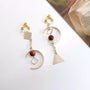 Geometric Harmony Dangle Clip-On Earrings in gold with burgundy beads and mixed metal shapes on white background