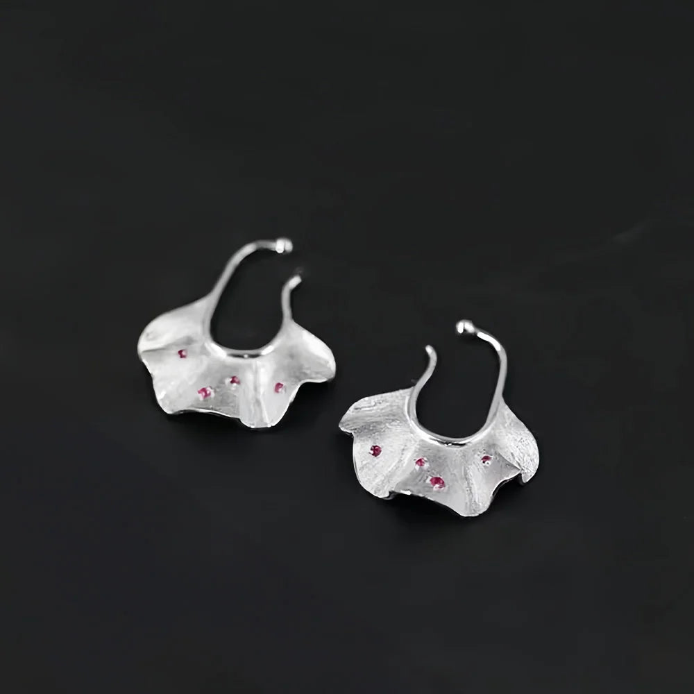 Silver ginkgo leaf ear cuff earrings with ruby accents, front view on black background