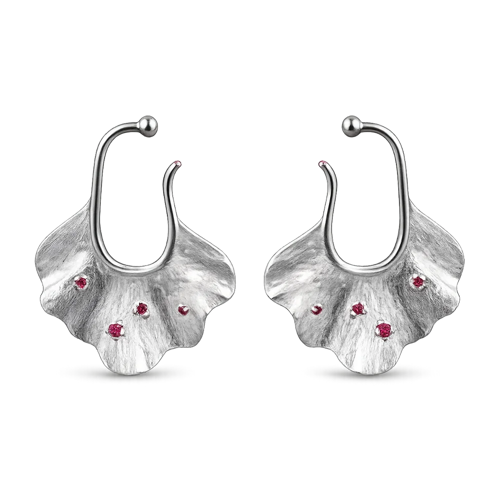 A pair of silver-toned huggie hoop earrings with a textured, organic leaf-like silhouette and small red gemstone accents, shown on a clean white background.