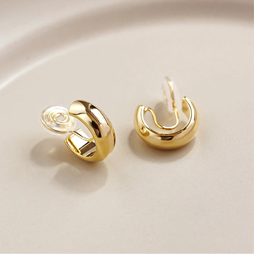Glossy gold clip-on hoop earrings displayed on white surface, showcasing polished finish and curved design from angled view