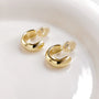Glossy gold clip-on hoop earrings displayed on white ceramic dish, showing polished finish and curved design from above