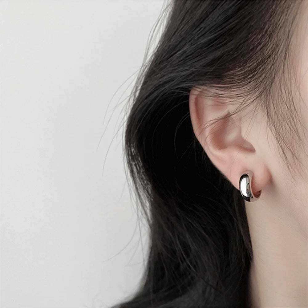 Glossy silver clip-on hoop earrings side view worn on ear against white background