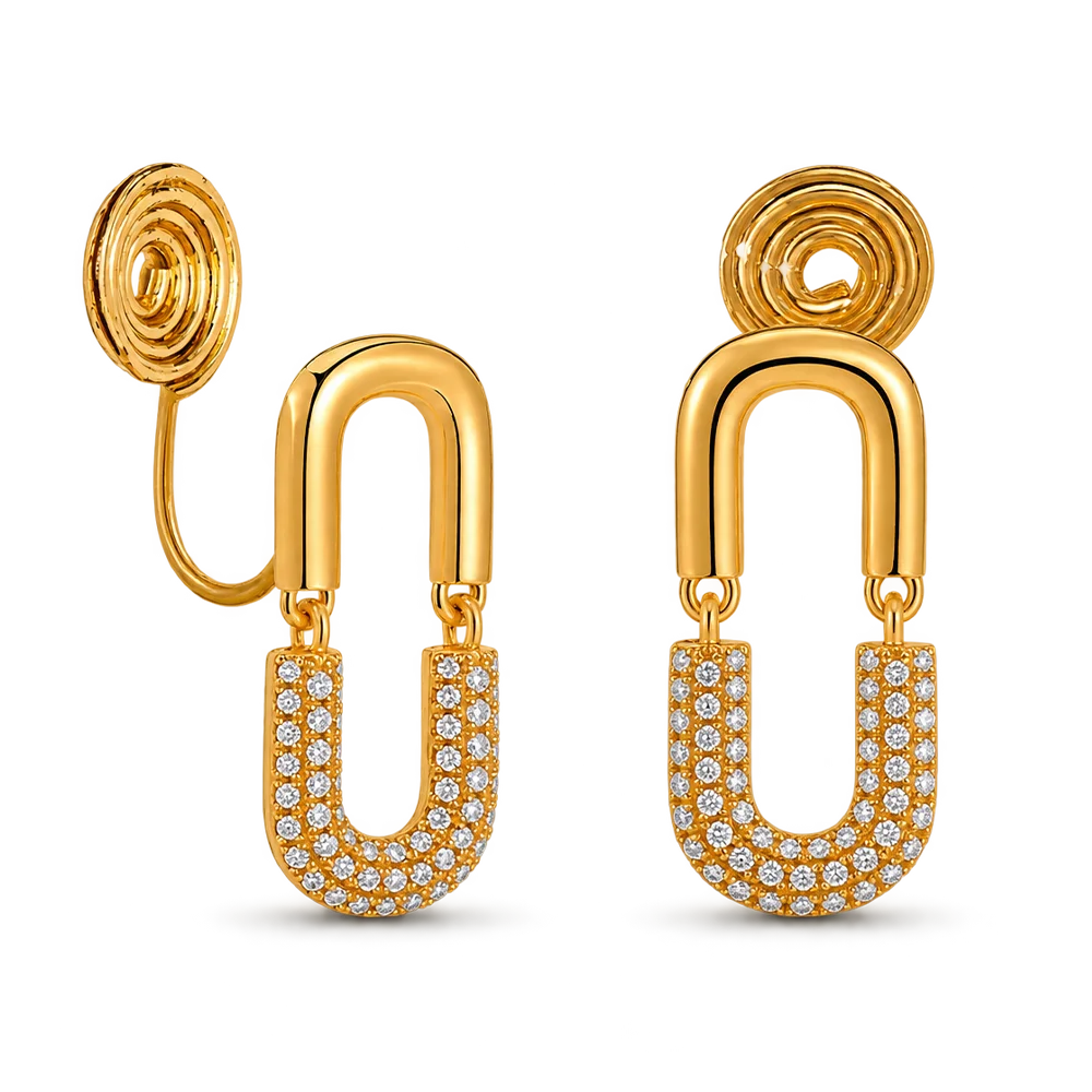 A pair of gold statement clip on earrings featuring a U-shaped drop, and a lower U-shaped section paved with small clear stones, shown on a white background.