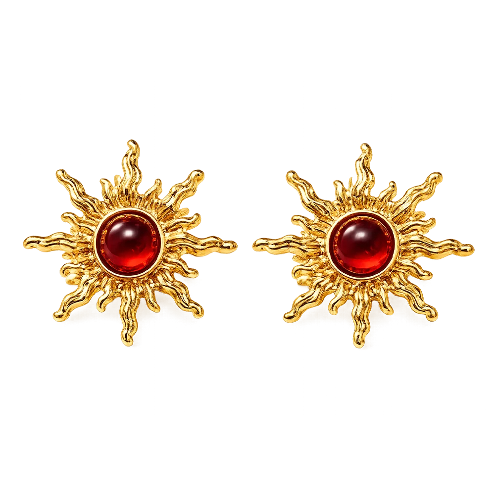 A pair of gold sunburst stud earrings with a polished round red cabochon gemstone in the center, set against a plain white background.