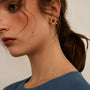 A close-up lifestyle shot of a woman wearing a gold-toned starburst earring with a red center gemstone. 