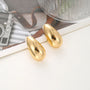 Chunky drop clip-on earrings in gold displayed on white surface with vintage camera and styling props