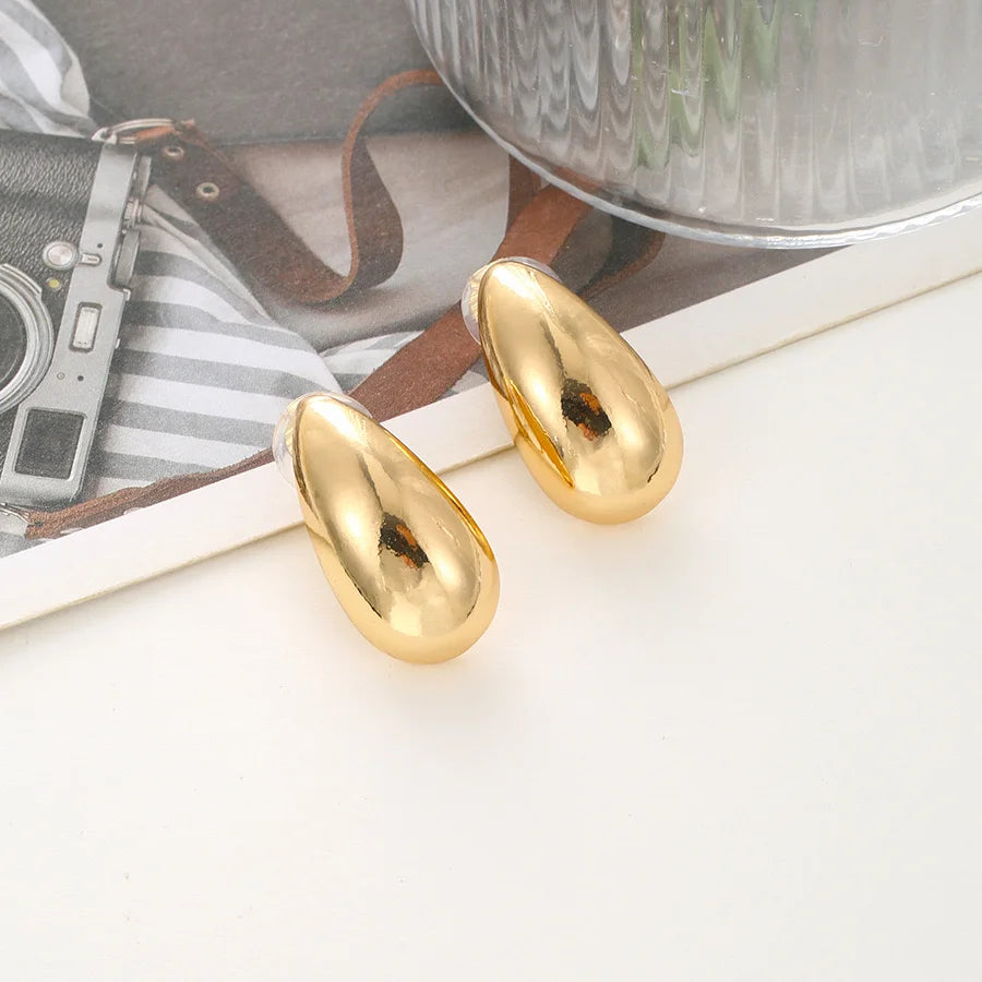 Chunky drop clip-on earrings in gold displayed on white surface with vintage camera and styling props