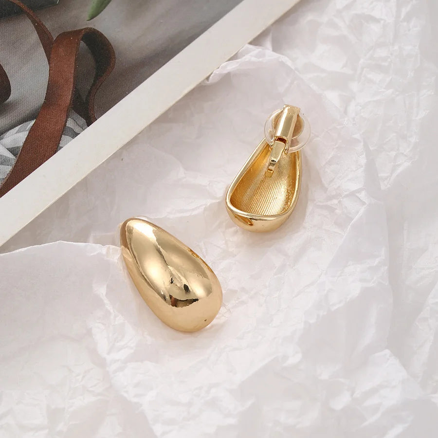 Gold chunky drop clip-on earrings displayed on white textured surface showing front and side angles