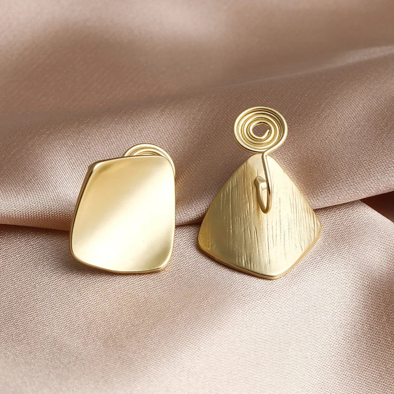 Gold square geometric clip on earrings displayed front and back view on beige fabric background