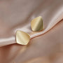 Gold square geometric clip on earrings displayed on beige fabric showing polished metallic finish and modern chunky design