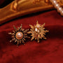 Gold sun clip-on earrings with pearl displayed on red velvet, showing front and back views of the ornate design
