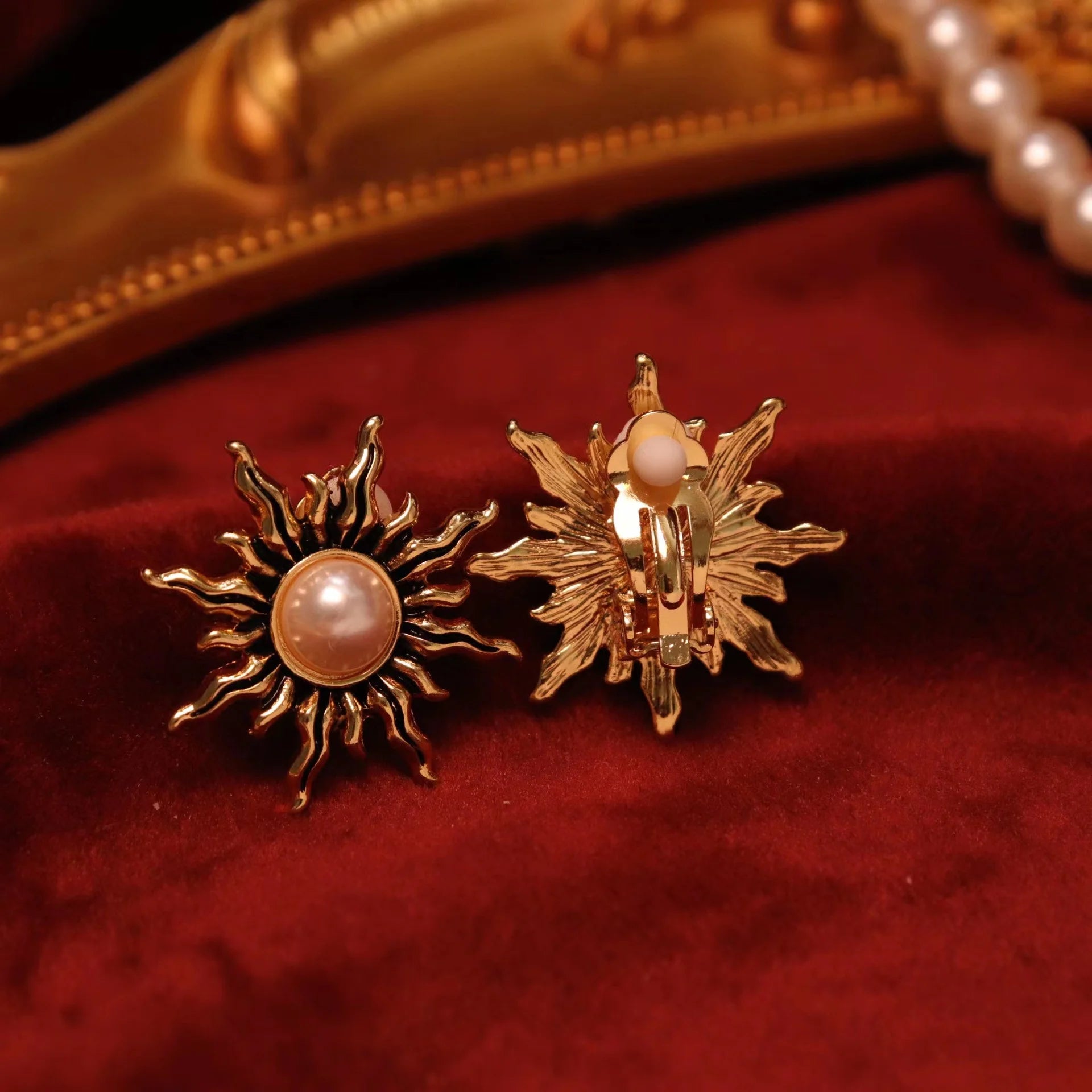 Gold sun clip-on earrings with pearl displayed on red velvet, showing front and back views of the ornate design