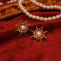Gold sun clip-on earrings with pearl centers displayed on red velvet with pearl necklace and jewelry in background