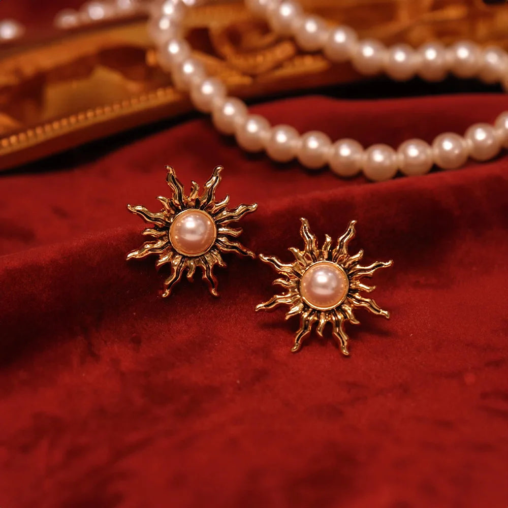 Gold sun clip-on earrings with pearl centers displayed on red velvet with pearl necklace and jewelry in background