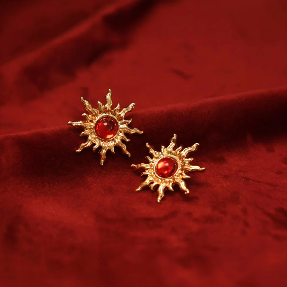 Gold Sun Clip-On Earrings with Ruby displayed on red velvet fabric, showing detailed front view of the sun-shaped design with red gemstone centers