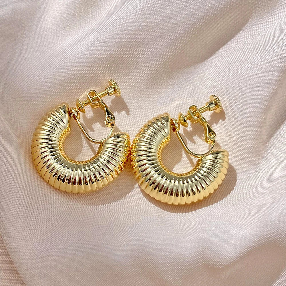 Gold helix hoop clip-on earrings displayed on white fabric, showcasing textured ribbed design from above