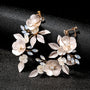 Golden Leaf & Blossom Clip-On Earrings with Pearls displayed on black sparkly background, showcasing delicate white floral design with pearl accents