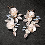 Golden Leaf & Blossom Clip-On Earrings with Pearls overhead view on dark background, featuring white floral petals and blue gemstone accents