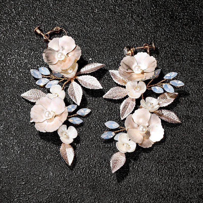 Golden Leaf & Blossom Clip-On Earrings with Pearls overhead view on dark background, featuring white floral petals and blue gemstone accents
