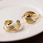 Gold rotating spiral clip-on hoop earrings displayed on white ceramic dish, showing textured twisted design from front angle