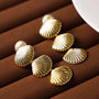 Gold textured shell clip-on earrings displayed on brown fabric, showcasing shiny metallic finish and detailed ridged design from above