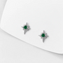 A pair of silver-toned starburst stud earrings with round green gemstones, displayed on a clean white surface.
