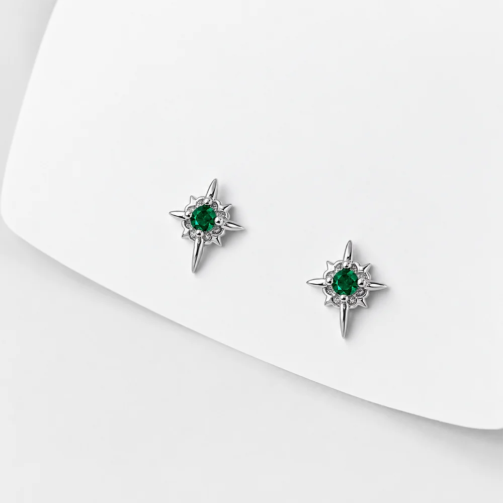 A pair of silver-toned starburst stud earrings with round green gemstones, displayed on a clean white surface.