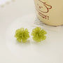Green flower clip-on earrings displayed on white surface with inspirational mug in background